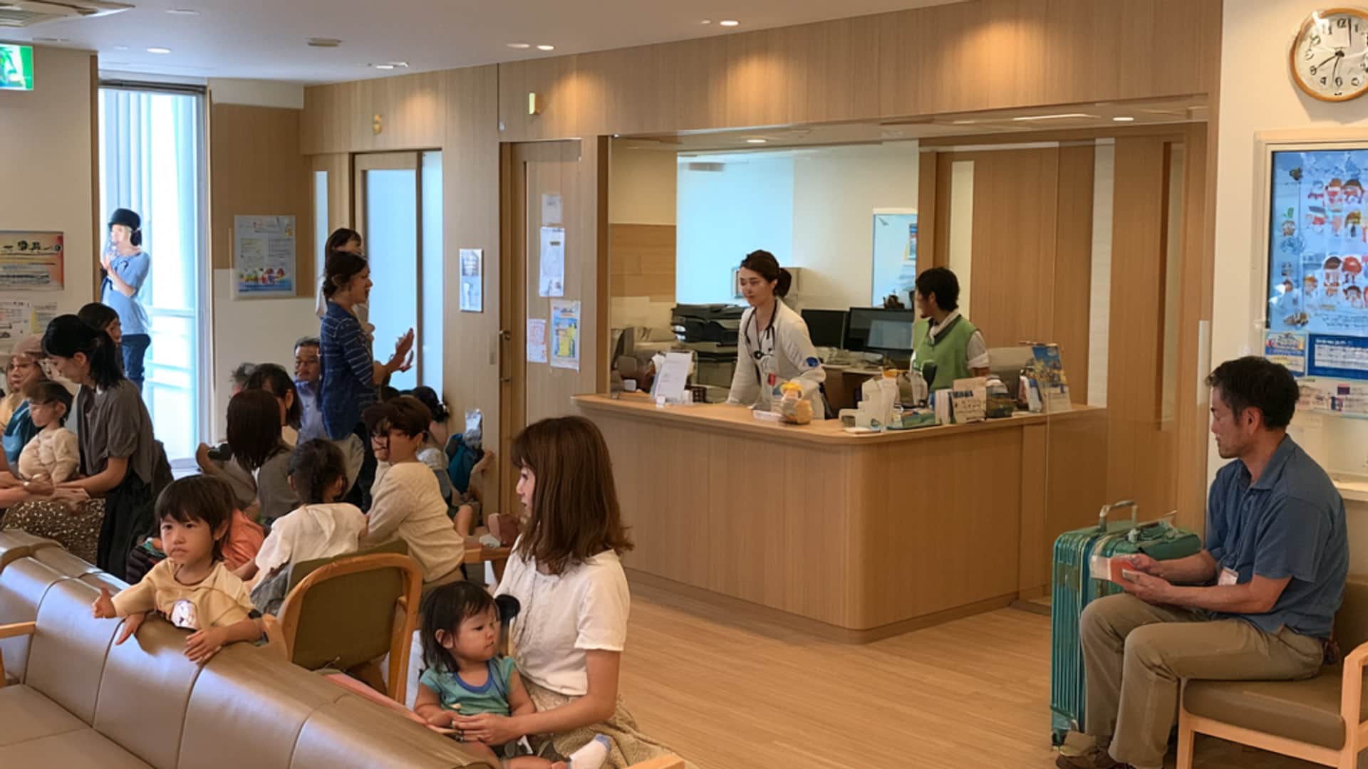 待合。木の椅子とソファが並び、受付カウンターの前で親子が順番を待っている